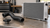 A generic radiator cap, curved coolant hose and compact radiator arranged separately on a workshop bench.